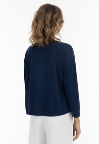 Marineblaues Langarmoberteil mit lockerem Schnitt, Rundhalsausschnitt und gerippten Bündchen, kombiniert mit weißen Hosen, die eine glatte Textur aufweisen.