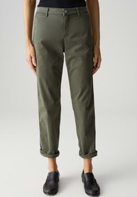 Pantaloni tapered in cotone misto verde oliva con orli arrotolati, chiusura anteriore con bottone e tasche laterali, abbinati a scarpe nere slip-on.