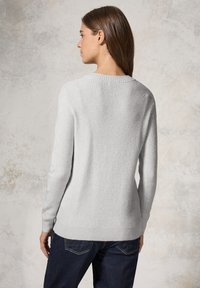 Maglione lavorato a maglia grigio chiaro con texture a costine, scollatura rotonda e maniche lunghe, indossato con jeans scuri. Vista posteriore che mette in risalto la vestibilità.