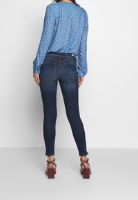 Blå mönstrad blus med långa ärmar, ihopparad med mörka denim skinny jeans och bruna blockklacksandaler. Jeans med slitna detaljer.