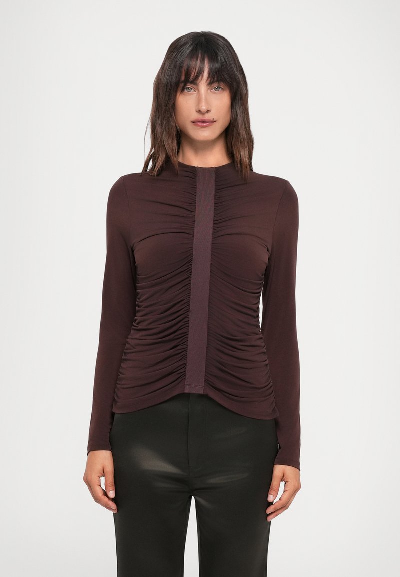 Mauve long-sleeve top with gathered detailing at sides and a vertical ribbed accent down the center; fabric appears smooth and fitted.