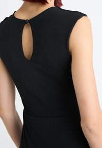 Zwarte jurk met kapmouwen, sleutelgatdetail op de rug bevestigd met een knop, zachte stof, getailleerd ontwerp, gladde textuur.