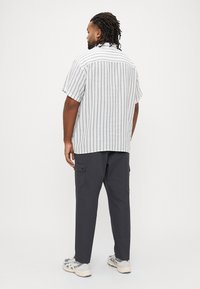 Κοντομάνικο, ριγέ πουκάμισο από ελαφρύ ύφασμα με κάθετες γραμμές. Συνδυασμένο με σκούρο παντελόνι τύπου cargo με πλαϊνές τσέπες και αθλητικά παπούτσια.