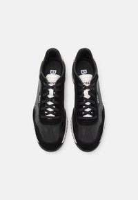 Chaussures de sport noires avec des empiècements en daim et synthétiques, dotées de lacets blancs, de textures lisses, et du nom de la marque "BOSS" sur la languette et les côtés.