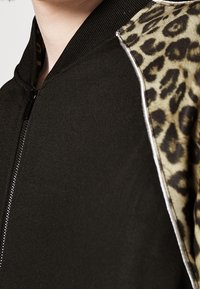 Bomber jacket nera con maniche in stampa leopardata. Presenta una chiusura con zip e colletto a coste. Il materiale appare liscio e ha una texture morbida.