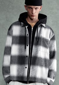 Siva i bijela flanel košulja jakna s velikim karo uzorkom, s crnim gumbima, džepom na prsima i slojevitom crnom kapuljačom ispod.