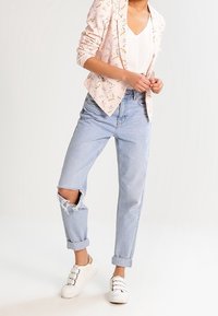 Lys rosa floral blazer over en hvid top, parret med slidte lys blå jeans med et revet knæ og opbrettede manchetter, complemented af hvide sneakers.