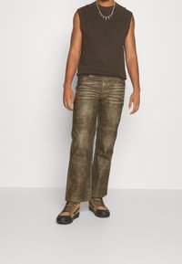 Grönbruna, vida byxor med en något sliten textur och synliga sömmar, i kombination med en ärmlös brun topp och snörboots.