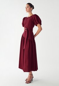 Bordeaux midi-jurk met pofmouwen, ceintuurband rondom de taille, met een ronde hals en geplooide rok; gestyled met zwarte hoge hakken.