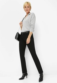 Pull en maille gris avec un col, associé à un pantalon noir ajusté et des bottines noires à bout pointu. Modèle tenant un petit sac noir.