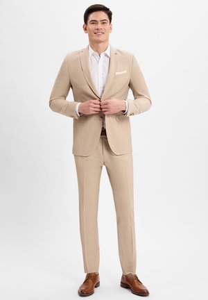 Lichtbeige pak met slim-fit ontwerp, met notched lapels, enkele knoopsluiting, gecombineerd met een wit shirt en bruine leren schoenen.