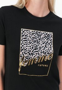 Black t-shirt featuring a leopard print design in a rectangular shape. Gold foil lettering displays "femme FUTURE" at the bottom.