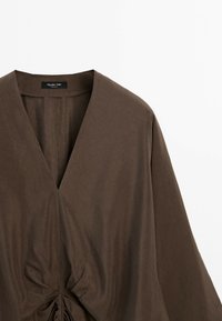 Brown long-sleeve top with deep V-neck and gathered knot detail at the front, hanging on a plain white background.