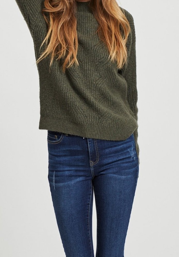 Pull en maille vert olive avec un col rond, associé à un jean skinny bleu foncé présentant un léger délavage et un design à cinq poches.