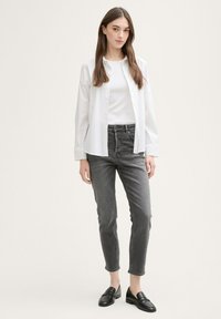 Camisa blanca de botones sobre una camiseta sin mangas blanca, combinada con unos jeans gris de cintura alta y mocasines negros. Tela suave y diseño ajustado.