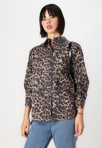 Leopard print button-up shirt in beige and black, smooth fabric, long sleeves, classic collar, paired with blue denim jeans. Black bag visible.