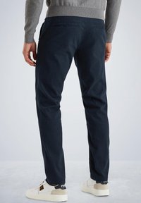 Pantalons en velours côtelé bleu marine à coupe slim, avec des poches arrières. Portés avec des baskets beiges et un pull gris, mettant en valeur le tissu texturé.