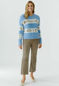 Lichtblauwe, pluizige trui met wit-grijs gestreept patroon; gecombineerd met beige suède flared broek en crèmekleurige schoenen met puntige neus.