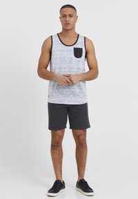 Débardeur sans manches blanc avec un motif texturé gris, poche noire, associé à un short gris foncé et des baskets noires.