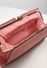 Roze nepleer handtas met een gouden metalen sluiting, voorzien van een satijnen interieur en een ritszak aan één kant.