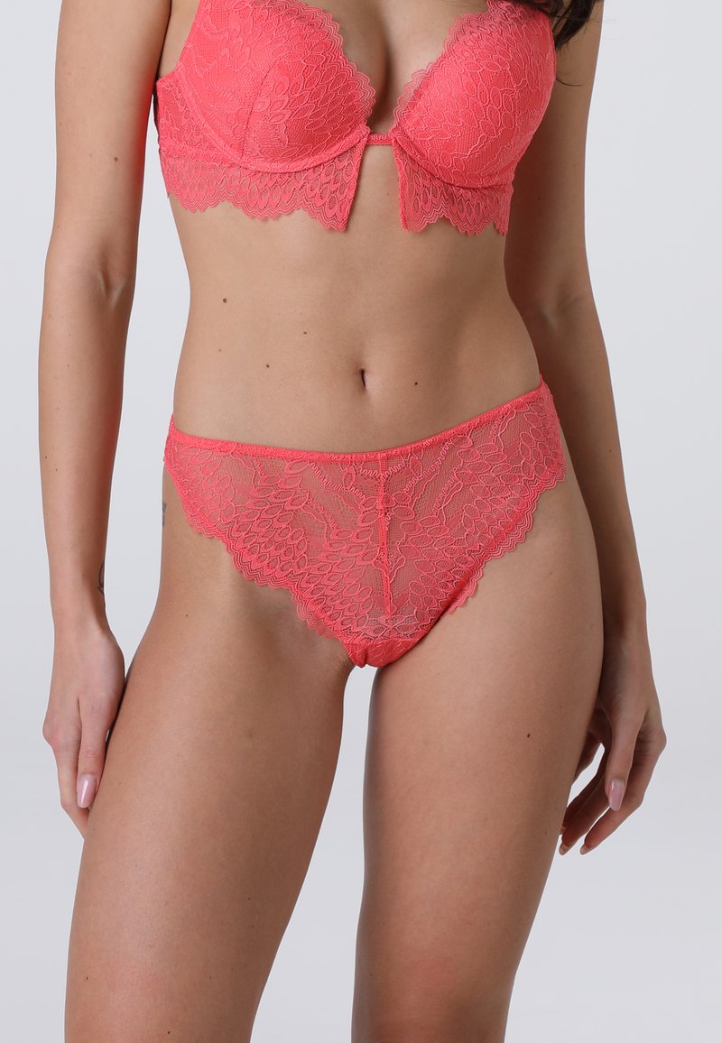 Set di lingerie in pizzo corallo composto da un reggiseno imbottito con bordi scallop e slip coordinati. Il tessuto è semi-trasparente con intricate fantasie floreali.