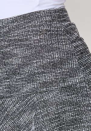 Melnā un baltā svītru auduma svārki ar teksturētu virsmu. Iezīmējas ar pieguļošu jostas daļu un nelielu logotipa akcentu sānos.