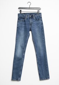Jean denim bleu, coupe slim, taille mi-haute, poches avant, délavage usé, ourlet net. Suspendu à un cintre noir avec clip.