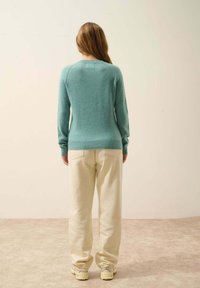 Pull en tricot bleu clair avec un col rond et des manches longues, associé à un pantalon large couleur crème, vu de dos.