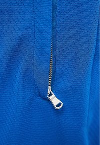 Tejido azul texturizado con una apertura con cremallera que presenta un tirador de cremallera plateado. La vista en primer plano enfatiza el patrón y los detalles del material.