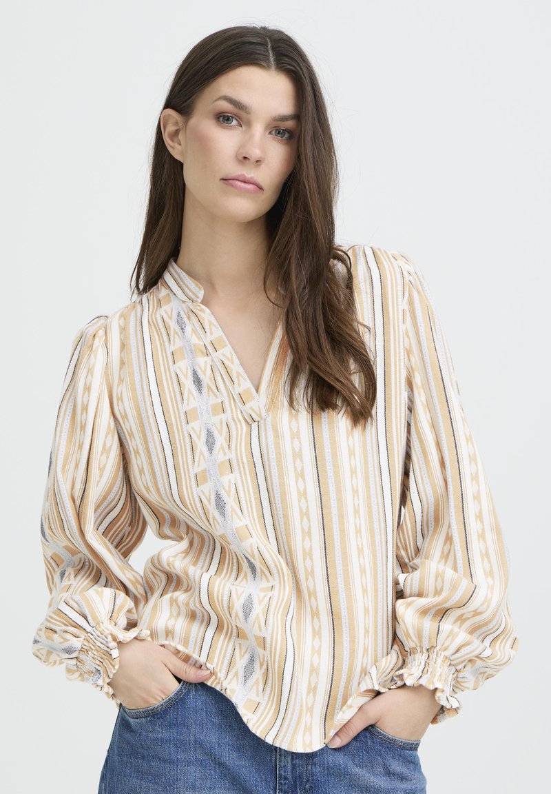 Blouse rayée présentant des motifs jaunes, blancs et gris, un décolleté en V et des poignets élastiqués. Confectionnée dans un tissu léger et texturé.