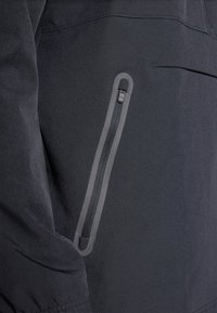 Zwarte jas met een zijzak met rits. Gemaakt van gladde stof, met een rits in grijsaccent en subtiele stikdetails. Minimalistisch ontwerp.