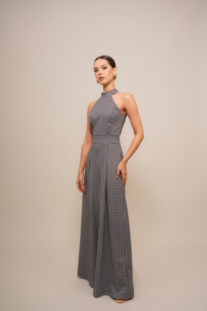 Svart og hvit houndstooth-mønstret maxikjole med halterneck, tettsittende liv og flytende skjørt. Glatt stofftekstur og utskjæringsdetaljer.