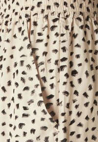 Béžová látka s nepravidelnými černými štětcovými skvrnami, ukazující elastický pas a otevření kapsy.