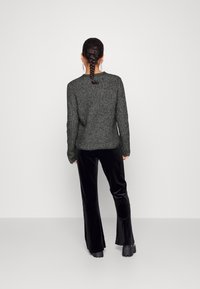 Tmavě šedý pletený svetr s kulatým výstřihem a dlouhými rukávy, doplněný černými sametovými kalhotami ve tvaru trumpet, viditelný ze zadní strany.