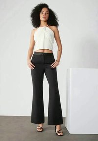 Top halter branco, cortado, com um design torcido, combinado com calças pretas de cintura alta e boca de sino. Sandálias pretas com tiras completam o visual.