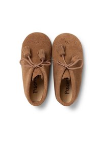 Zapatos de gamuza marrón en estilo moccasín con borlas y lazos decorativos. Textura suave y forma redondeada. El interior presenta el nombre de la marca.