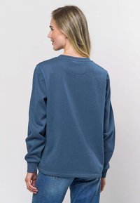 Zils kokvilnas džemperis ar garām piedurknēm, ribots apaļu kakla izgriezums un sānu šuves. Mugurai ir gluda tekstūra un neliela lejupejoša izliekuma apakšmala.