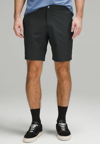 Czarne szorty wykonane z miękkiego materiału o gładkiej fakturze, z zapięciem na guziki i bocznymi kieszeniami. W zestawie z czarnymi trampkami i skarpetkami.