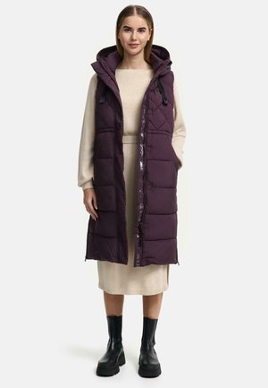 Lange, mouwloze, paarse puffer vest met een quilted patroon, een capuchon met trekkoord en een rits aan de voorkant. Gedragen over een crèmekleurige jurk.