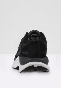Scarpa sportiva nera con tomaia in mesh, colletto imbottito e suola bianca con un motivo testurizzato. Presenta il marchio sul tallone.
