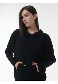 Schwarzer, gestrickter Kapuzenpullover mit lockerer Passform, ribbeliger Textur, vorderen Taschen und goldenen Beschlägen an den Kordeln.