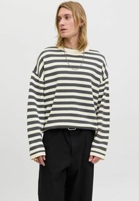 Striped sweater in cream and dark gray. Relaxed fit with long sleeves, dropped shoulders, and a rounded neckline. Paired with black trousers.