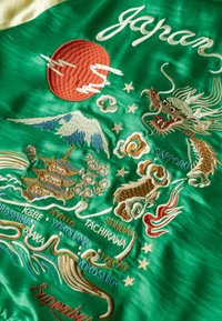 Veste bomber en satin vert ornée de broderies colorées de monuments japonais, d'un dragon, de fleurs de cerisier et du soleil, avec les noms des villes inclus.