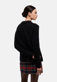 Pull noir en tricot avec col et poignets côtelés, assorti à une mini-jupe à carreaux. Le pull présente une coupe décontractée et légèrement oversize.