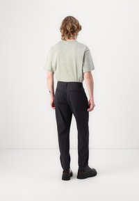 Ljusgrön bomullströja med korta ärmar, kombinerad med mörka, smalare byxor och svarta skor med tjock sula. Minimal design, inga synliga mönster.