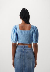 Crop top bleu clair avec des manches bouffantes, dos smocké et décolleté carré, associé à une jupe en jean taille haute avec deux poches arrière.