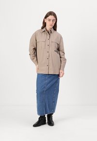 Beige gombos ing, két mellzsebbel, hosszú farmer szoknyával és fekete bokacsizmával párosítva. Simább anyag, laza fazonú.