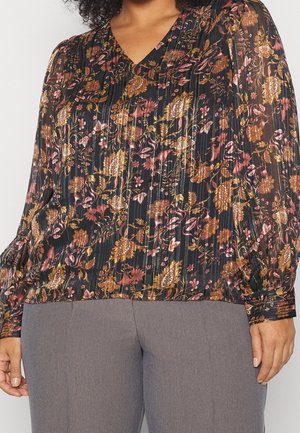 Bluse mit floralem Muster auf schwarzem Hintergrund, mit rosa und goldenen Mustern, plissiertem Design und langen Puffärmeln. Kombiniert mit grauen Hosen.