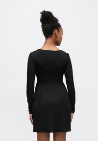Czarna sukienka z długim rękawem, dopasowaną górą i rozkloszowanym dołem. Gładka tekstura i prosty design, z okrągłym dekoltem i subtelnymi szwami.