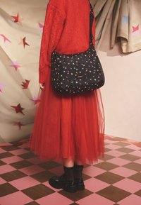 Borsa a tracolla nera con motivo di stelle multicolori, tracolla regolabile, piccolo dettaglio logo, abbinata a una gonna in tulle rossa e maglione lavorato a maglia.